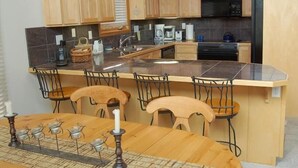 Una cucina con mobili in legno, un piano di lavoro in granito, un lavello, un fornello e un'area pranzo con tavolo e sedie.
