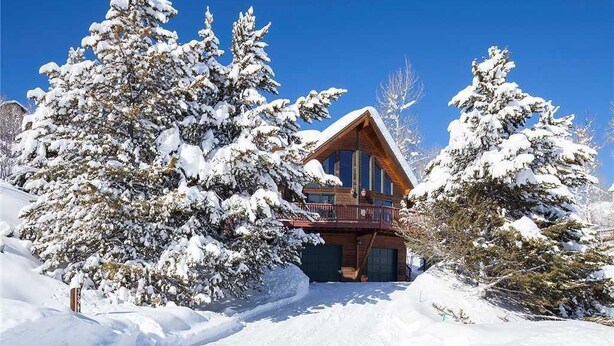 Una baita di legno con facciata in legno, circondata da alberi innevati e un cielo azzurro limpido.