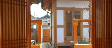 Una habitación japonesa tradicional con suelo de tatami, puertas correderas de madera y vistas a un patio con un edificio al fondo.