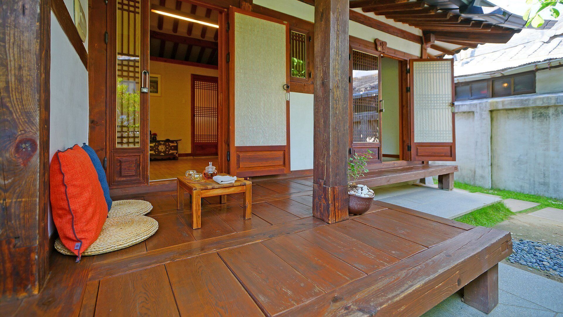 Un porche japonés tradicional de madera con esteras de tatami, una mesita con juego de té y un banco.