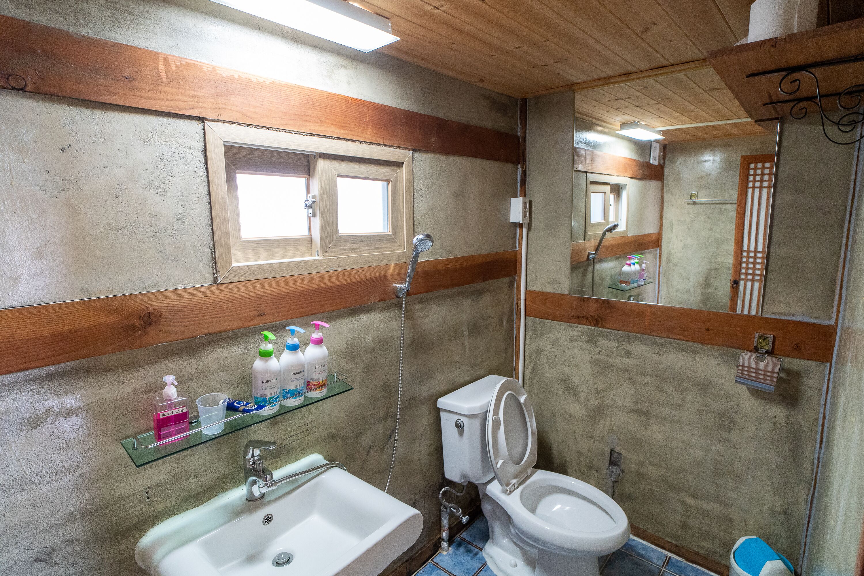 A bathroom with a sink, toilet, and shower. There is a window above the sink and a mirror above the toilet.