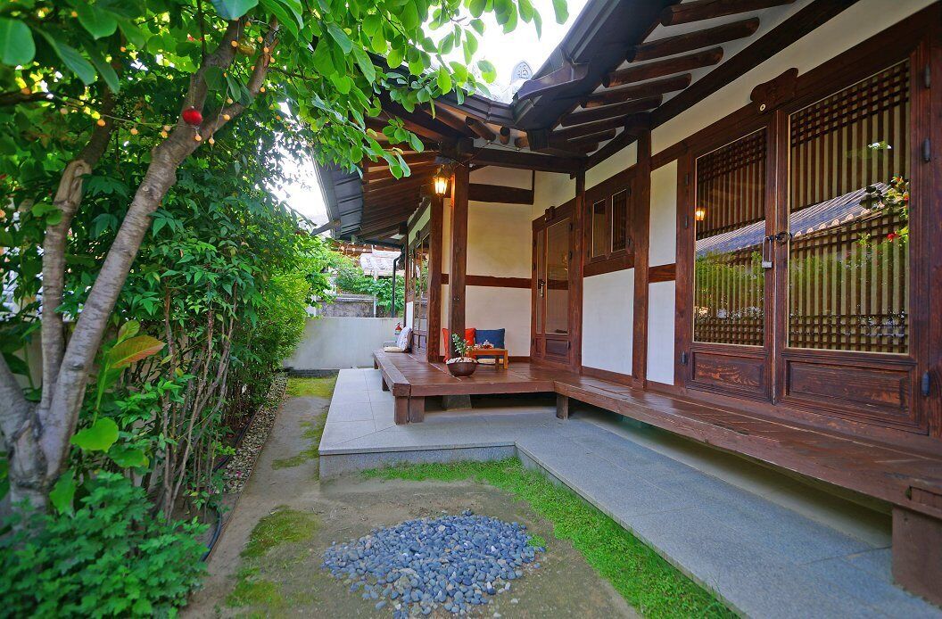 Een traditioneel Japans gebouw met een houten gevel, een overdekte veranda en een kleine tuin met kiezels en groen.