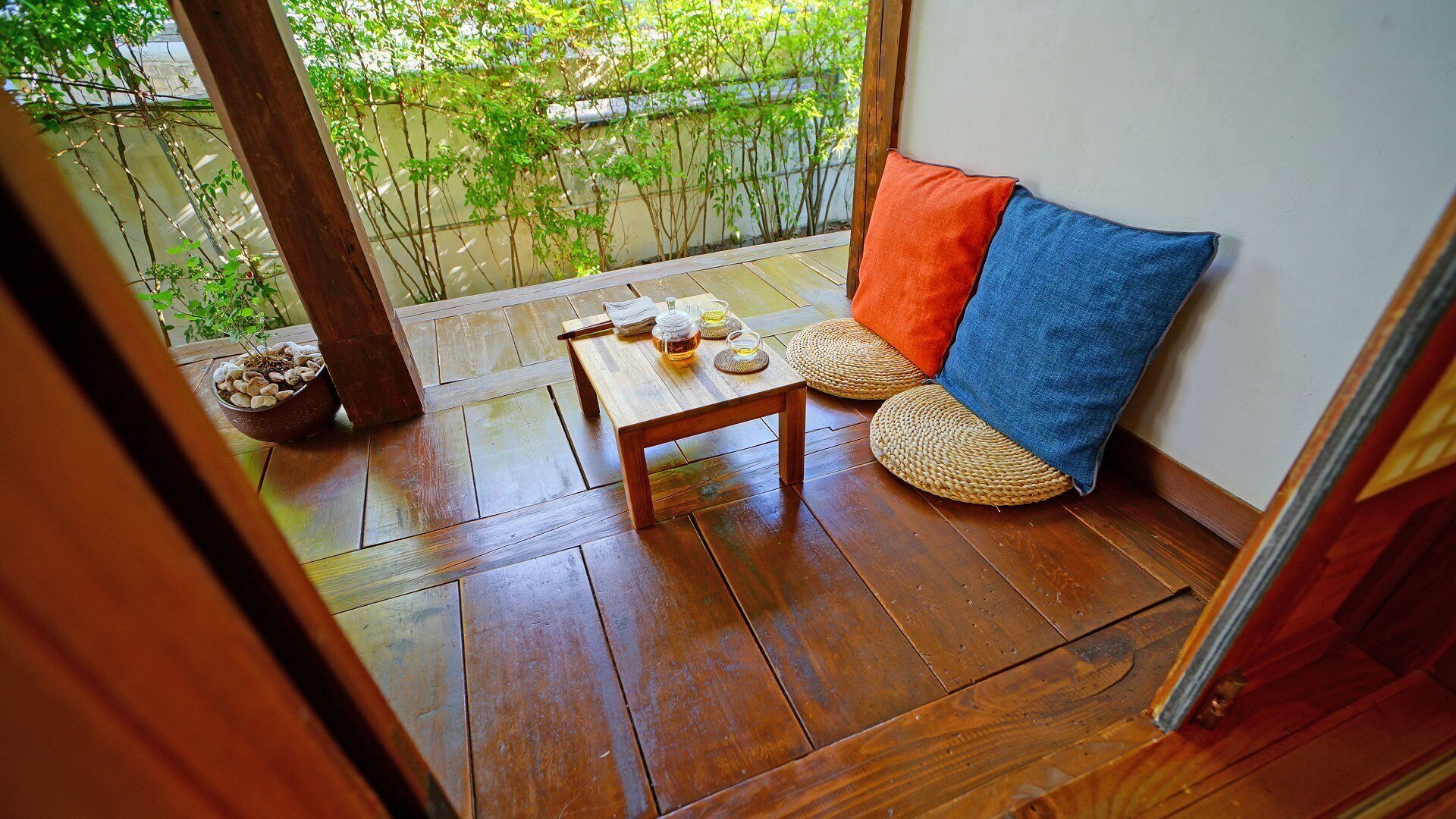 Una terraza de madera con una mesa, sillas, una planta en maceta y vistas a la vegetación.