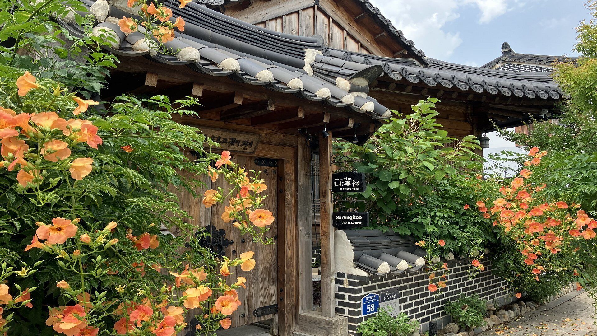 A traditional wooden building with a tiled roof, surrounded by lush greenery and orange flowers.