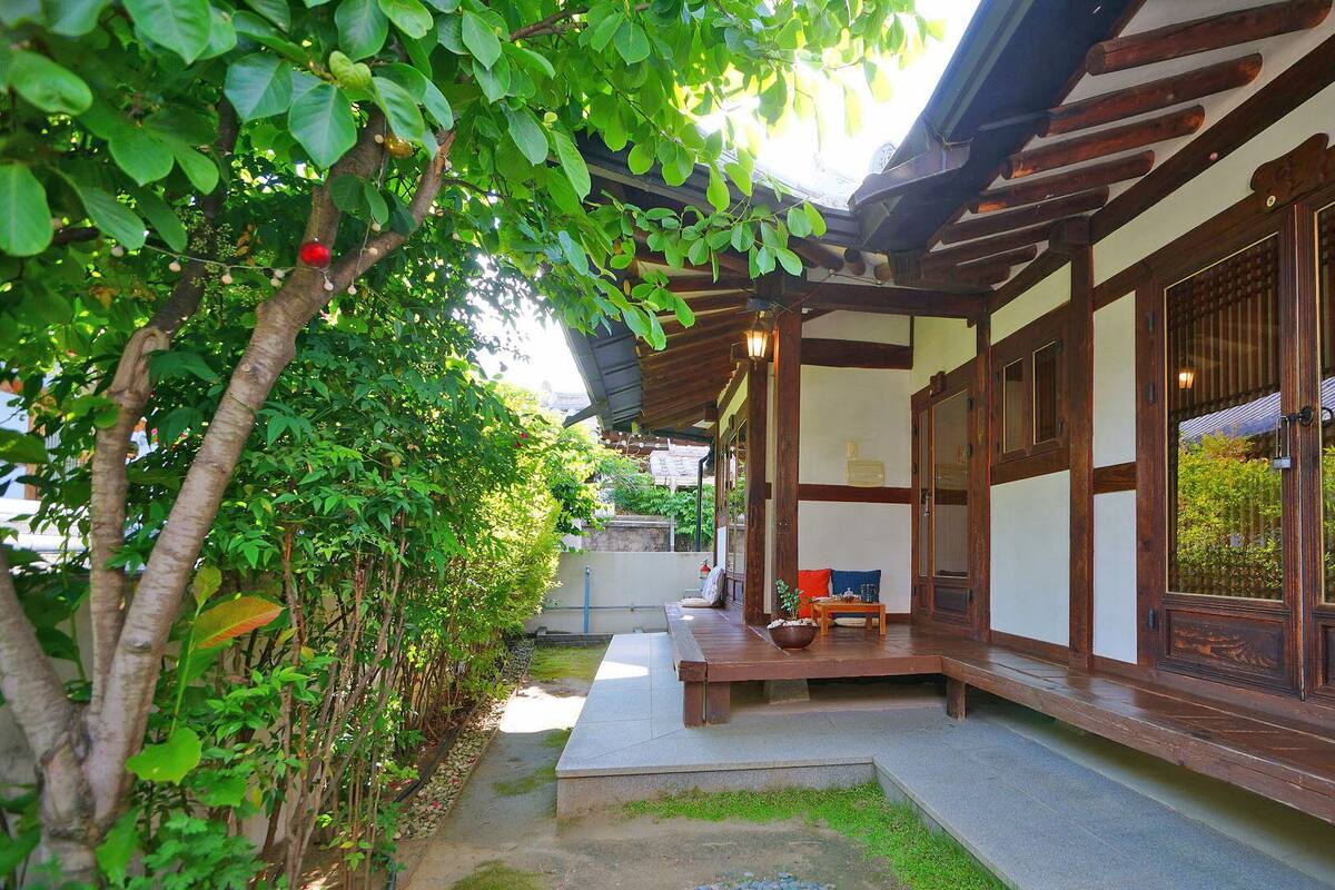 Un edificio tradicional japonés con fachada de madera, un porche cubierto y un pequeño jardín con un sendero.