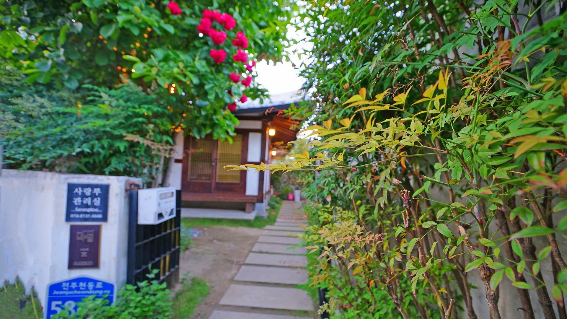 Un sentier mène à un bâtiment de style japonais traditionnel, doté d’une façade en bois et d’une entrée couverte.