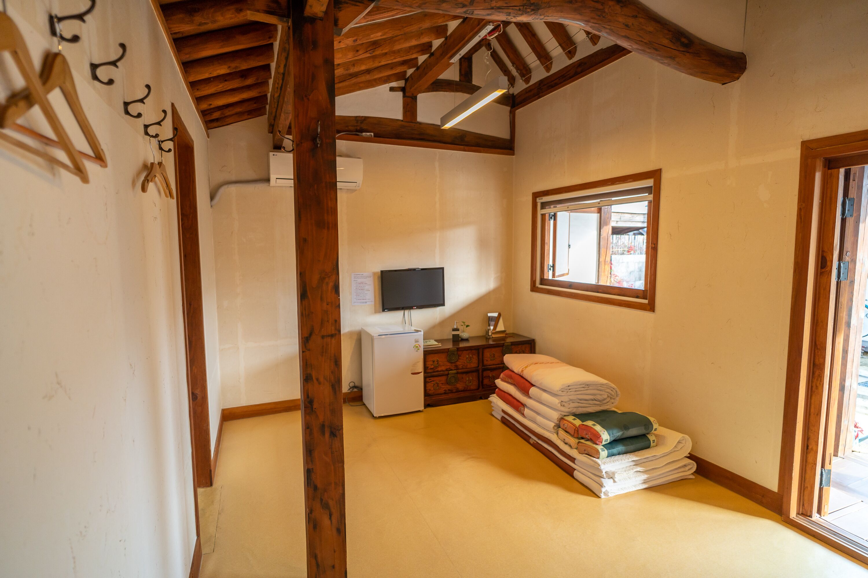 A room with wooden beams, a television, a small refrigerator, and a window with a view.