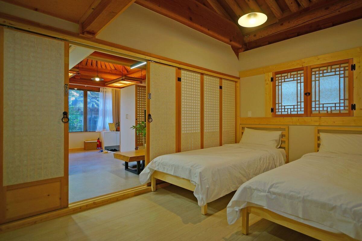 Una habitación japonesa tradicional con puertas correderas, dos camas individuales, una mesita y vistas al exterior a través de una ventana.