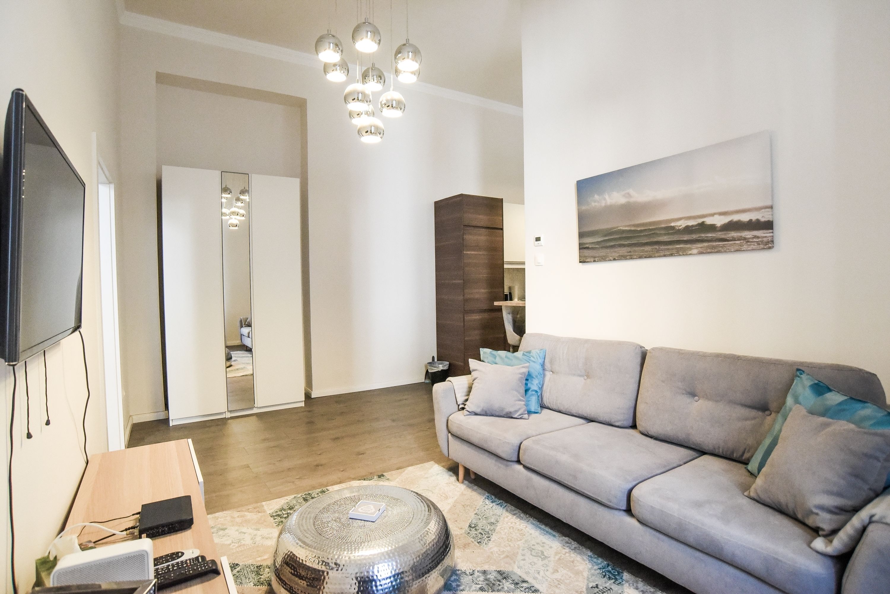 A modern living room with a grey sofa, a coffee table, a TV, and a painting of a beach scene.