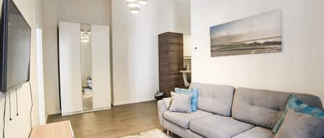 A modern living room with a grey sofa, a coffee table, a TV, and a painting of a beach scene.