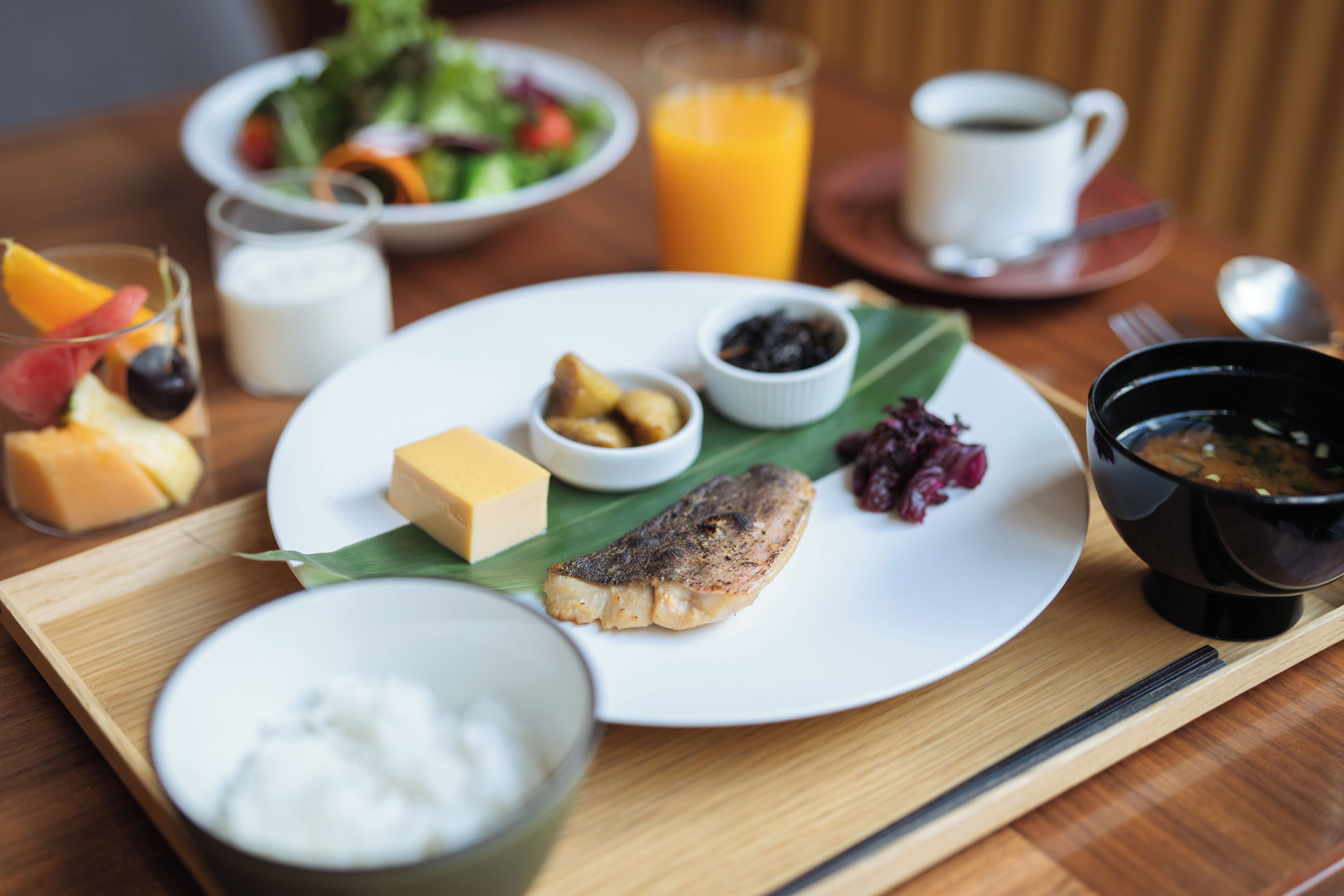 A breakfast setting with a plate of food, including a fish fillet, fruit, and condiments, on a wooden table.