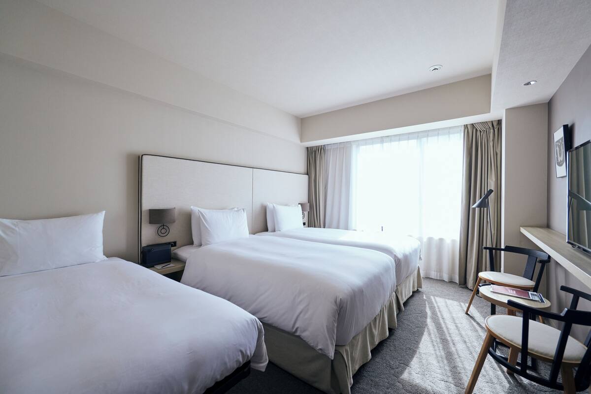 A hotel room with two beds, a desk, and a chair.