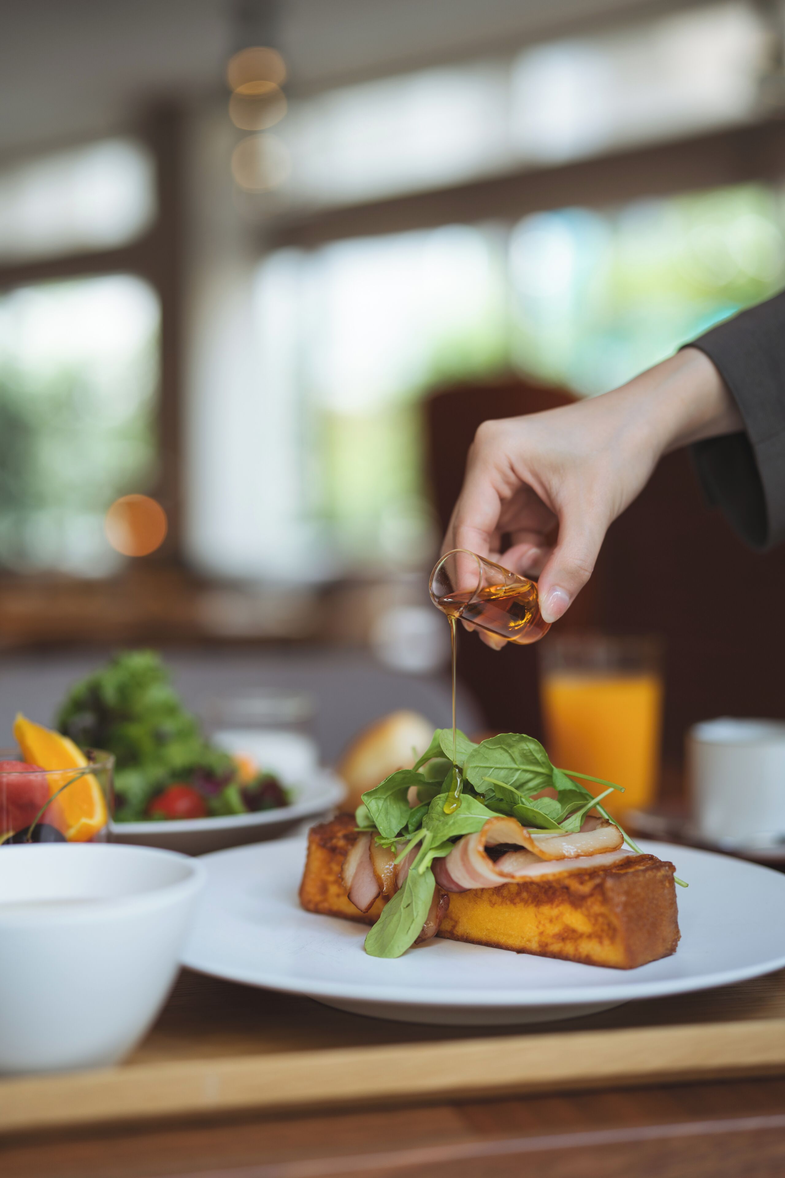 A breakfast setting with a plate of toast topped with greens and a hand pouring syrup.