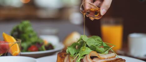 A breakfast setting with a plate of toast topped with greens and a hand pouring syrup.