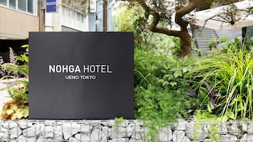 A NOHGA HOTEL sign with a stone wall and greenery in the foreground.