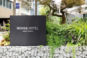 A NOHGA HOTEL sign with a stone wall and greenery in the foreground.