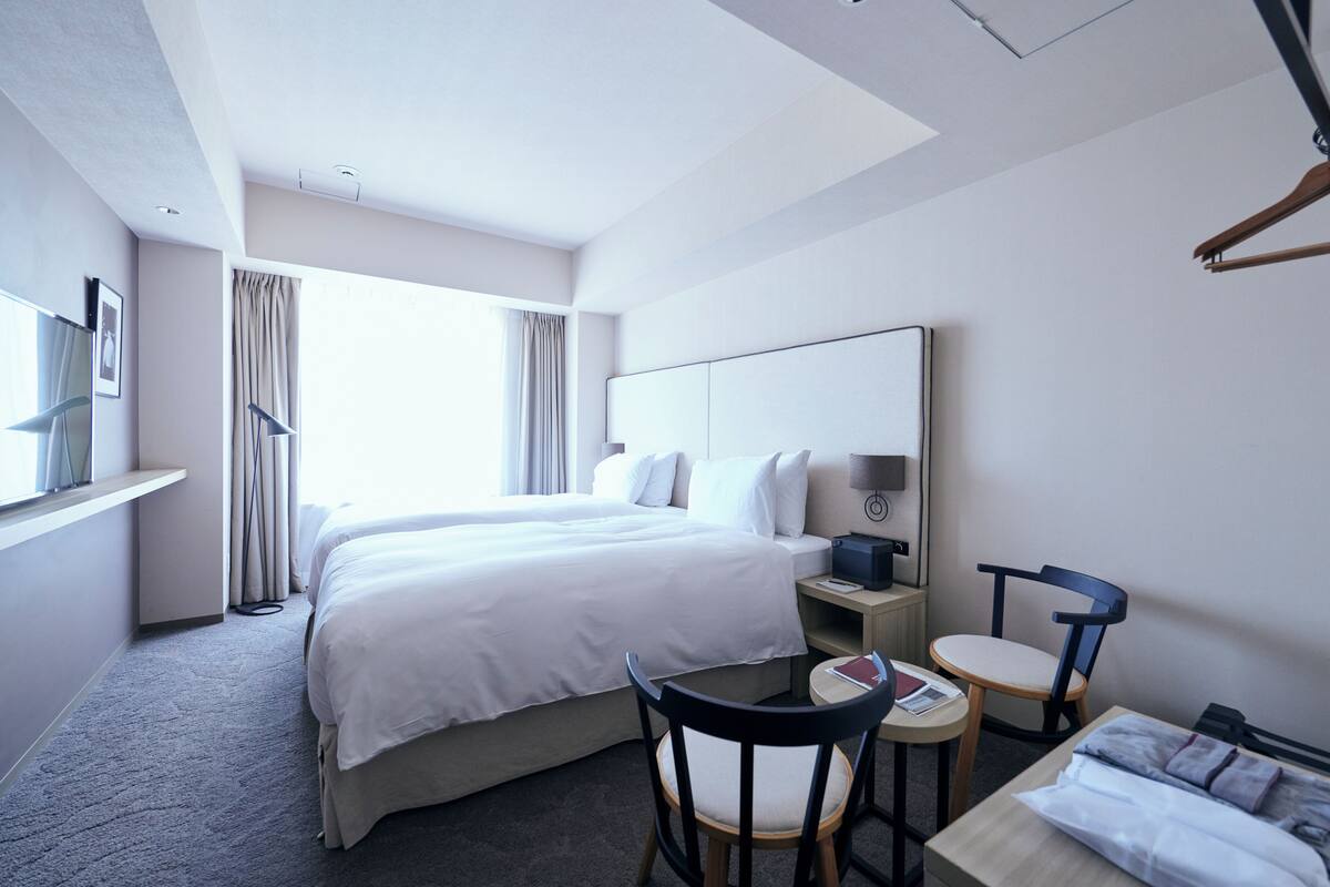 A hotel room with a large bed, a desk with a chair, a small table, and a wardrobe.