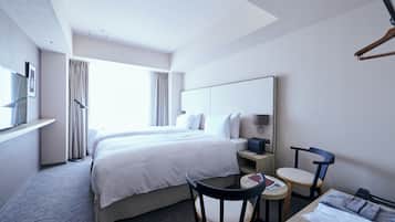 A hotel room with a large bed, a desk with a chair, a small table, and a wardrobe.