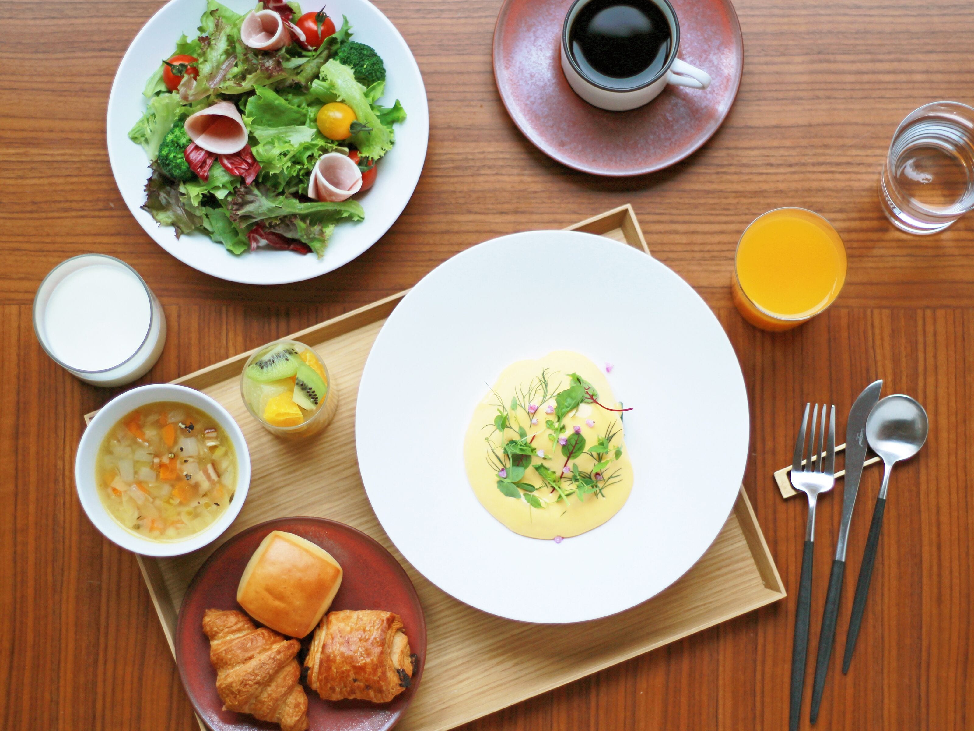 Una mesa de madera con una variedad de platos, incluyendo una ensalada, sopa y pasteles, junto con una taza de café y un vaso de zumo de naranja.