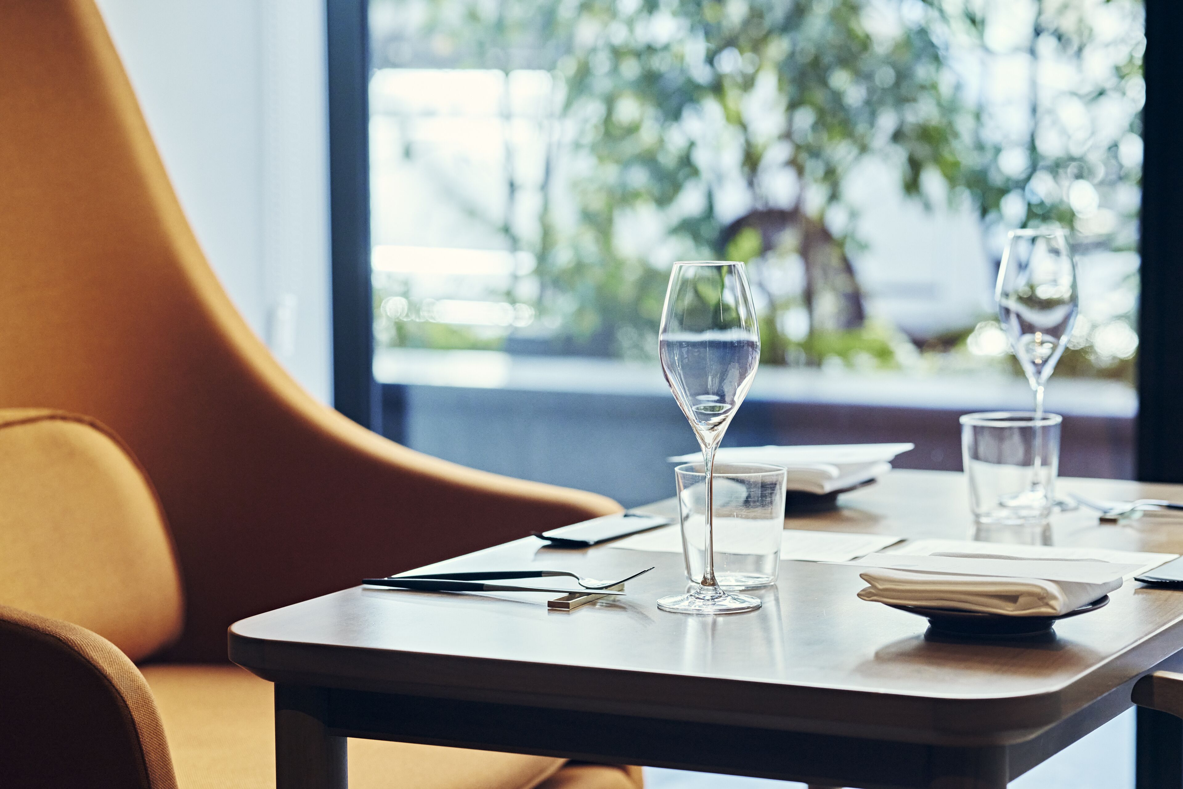 A dining table with a water glass and a folded napkin, a smartphone, and a pen.