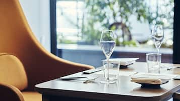 A dining table with a water glass and a folded napkin, a smartphone, and a pen.