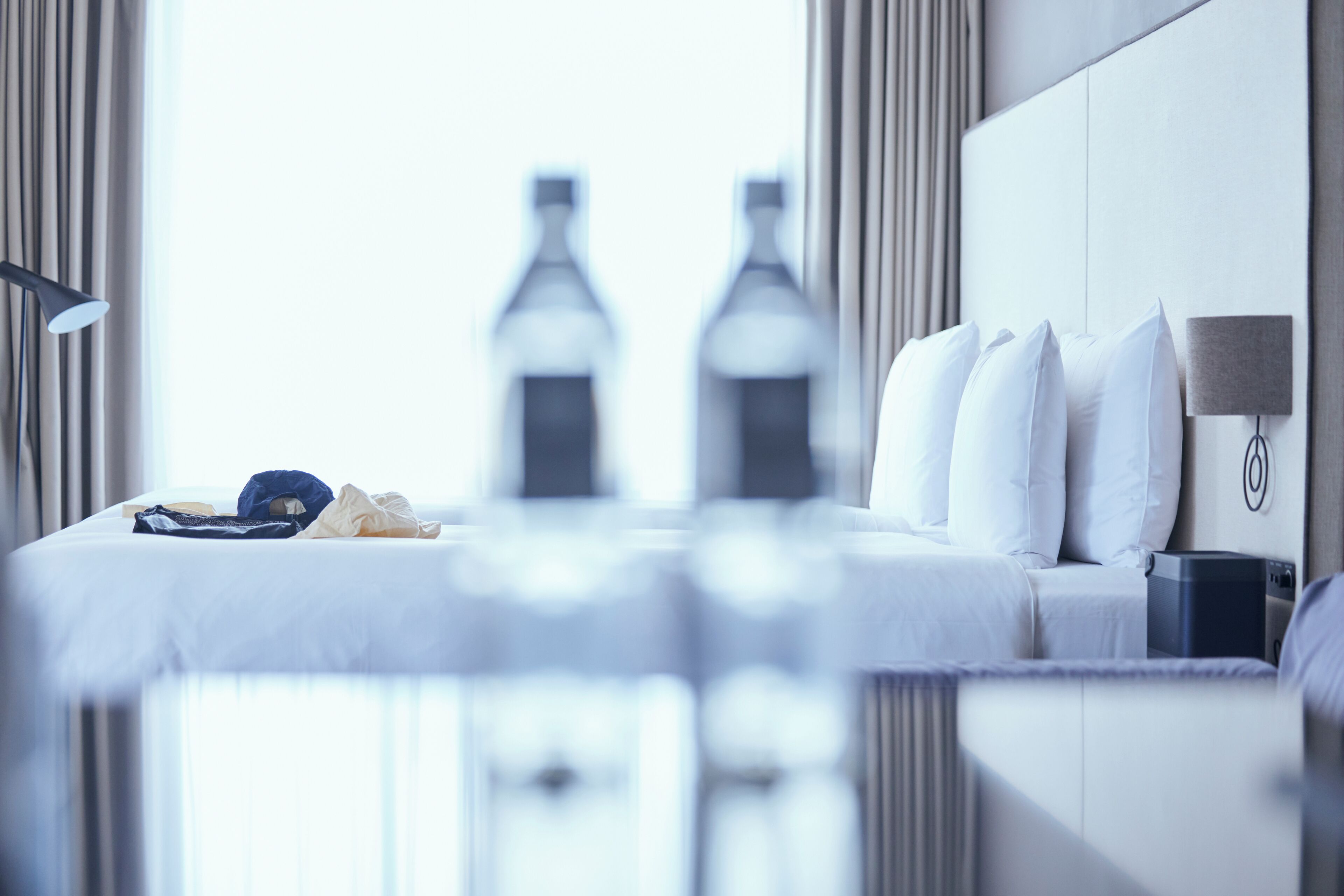 Een hotelkamer met een bed, nachtkastje, lamp en uitzicht op flessen buiten het raam.