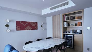 A modern dining area with a marble table and chairs, a red patterned wall hanging, and a built-in kitchen with shelves.