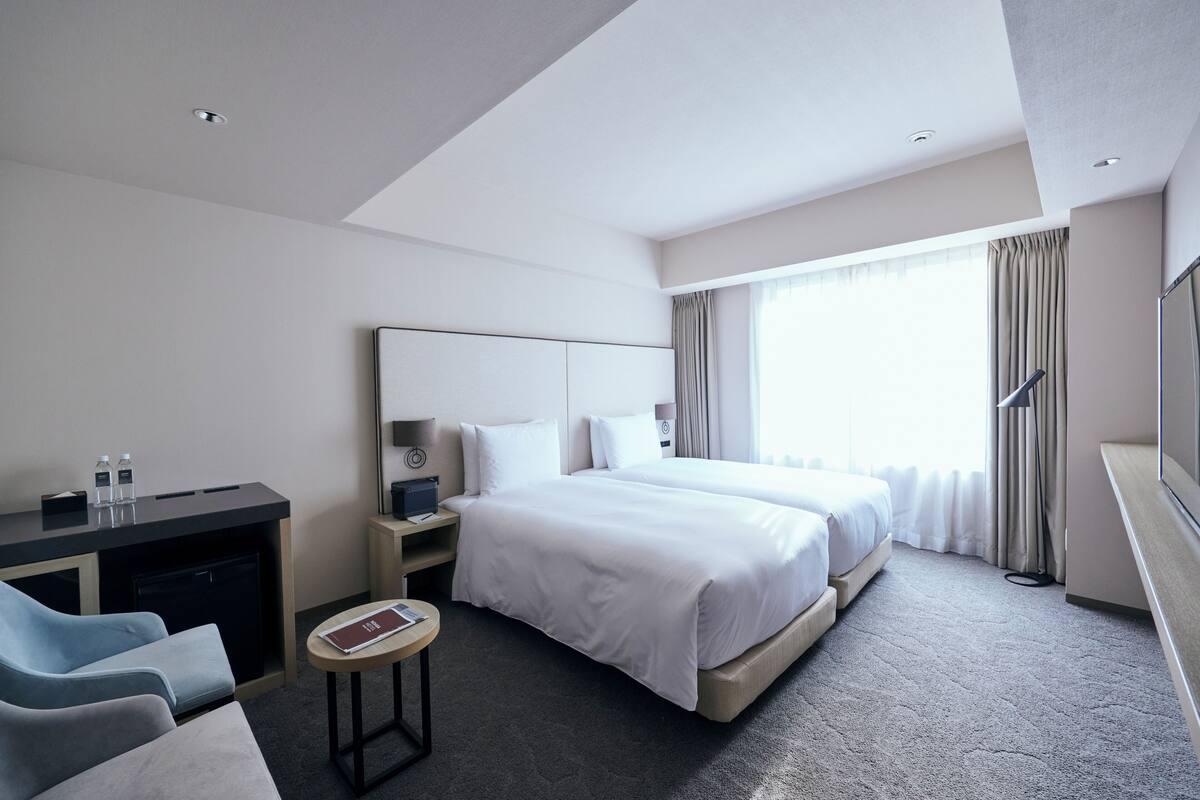 A modern hotel room with a large bed, a desk, a chair, and a small table.