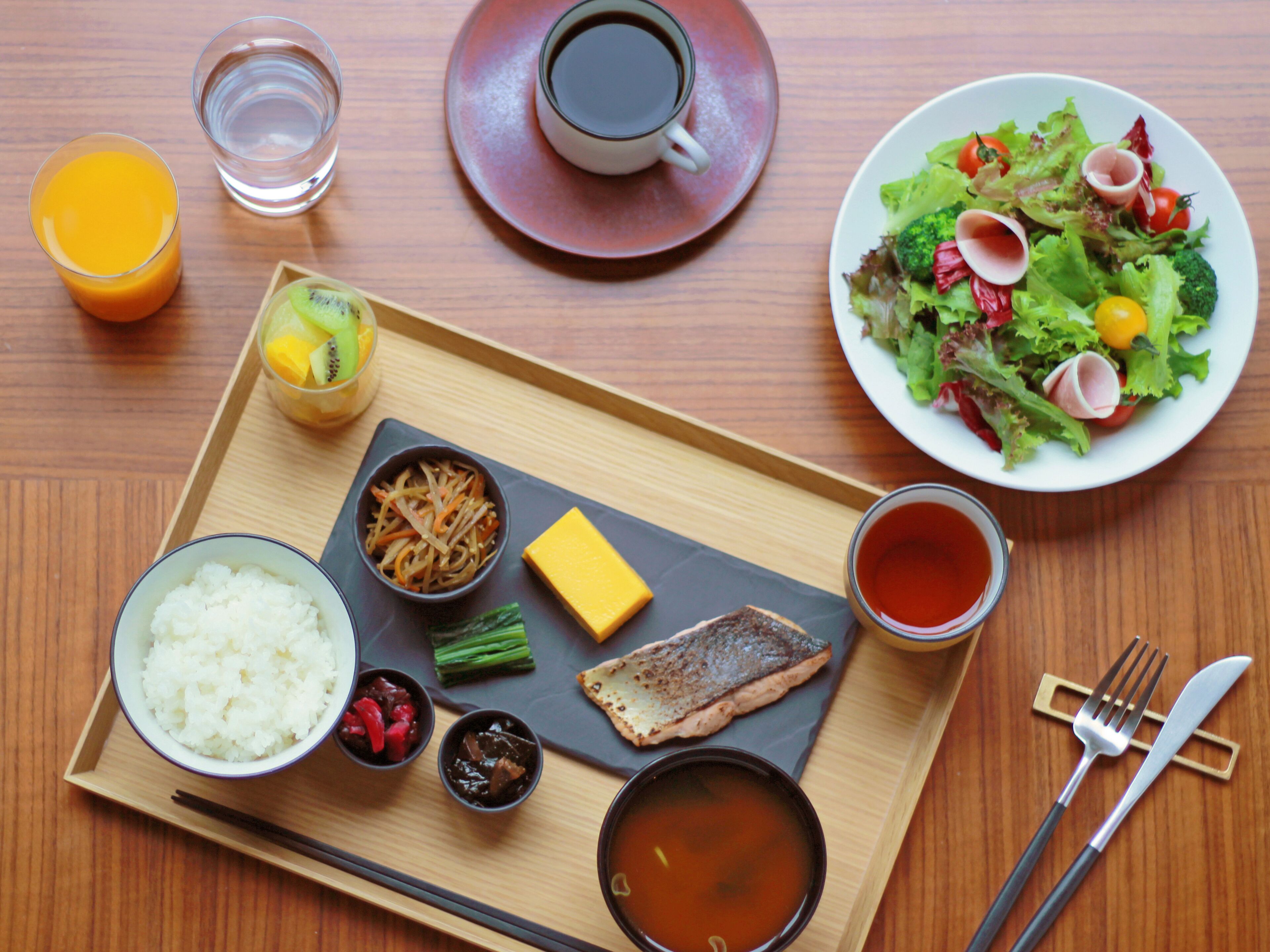 A tray with various dishes including rice, soup, and a fish, along with a plate of salad and drinks.