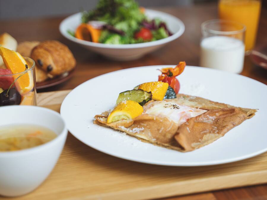 A breakfast setting with a plate of food, a bowl of soup, a croissant, a glass of orange juice, and a glass of milk.