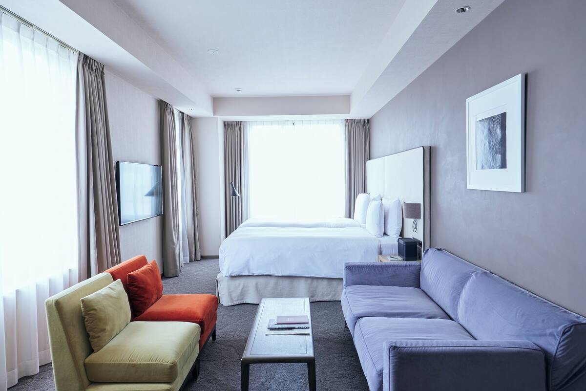 A hotel room with a bed, two sofas, a coffee table, a TV, and a large window with curtains.