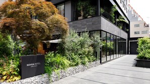 Una entrada moderna de hotel con una pared de piedra, abundante vegetación y un letrero del Hotel Nohga en Ueno, Tokio.