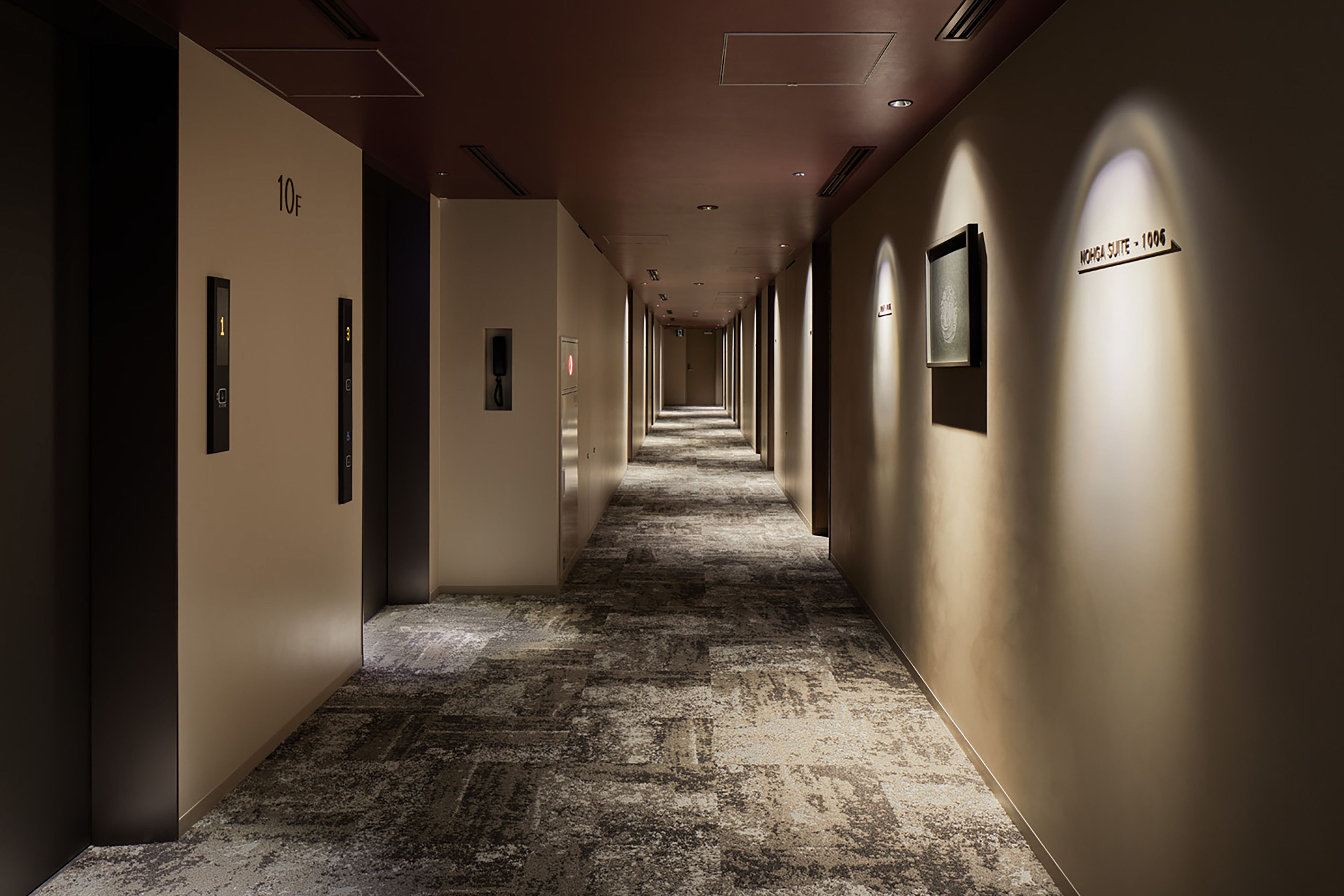 A long, narrow hotel corridor with a carpeted floor, walls with directional signs, and a ceiling with recessed lighting.