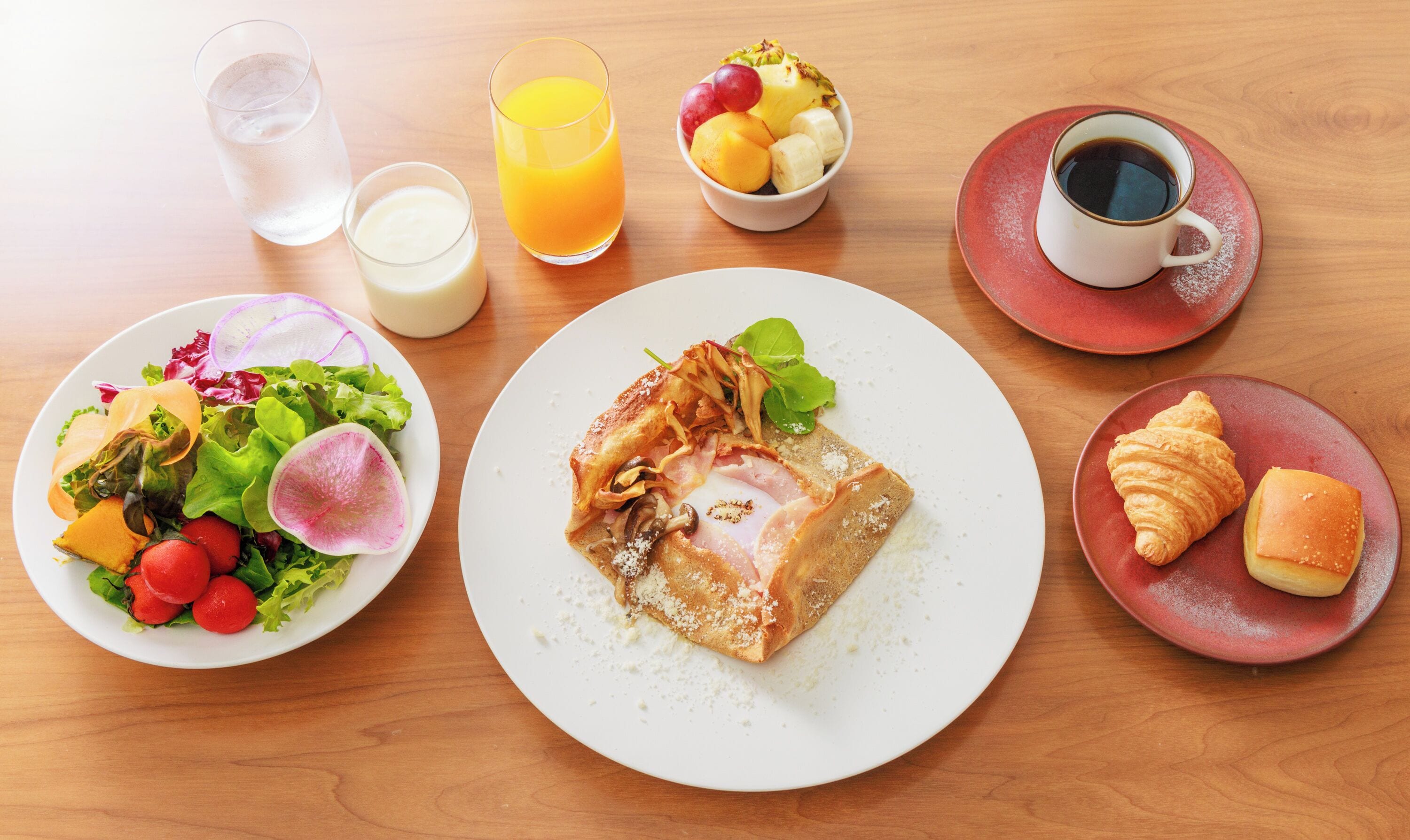 Una colazione con piatti di cibo, un bicchiere di succo d'arancia, una tazza di caffè e un bicchiere d'acqua.