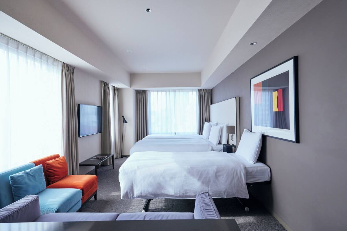 A modern hotel room with a large bed, a sofa, a TV, and a painting on the wall.