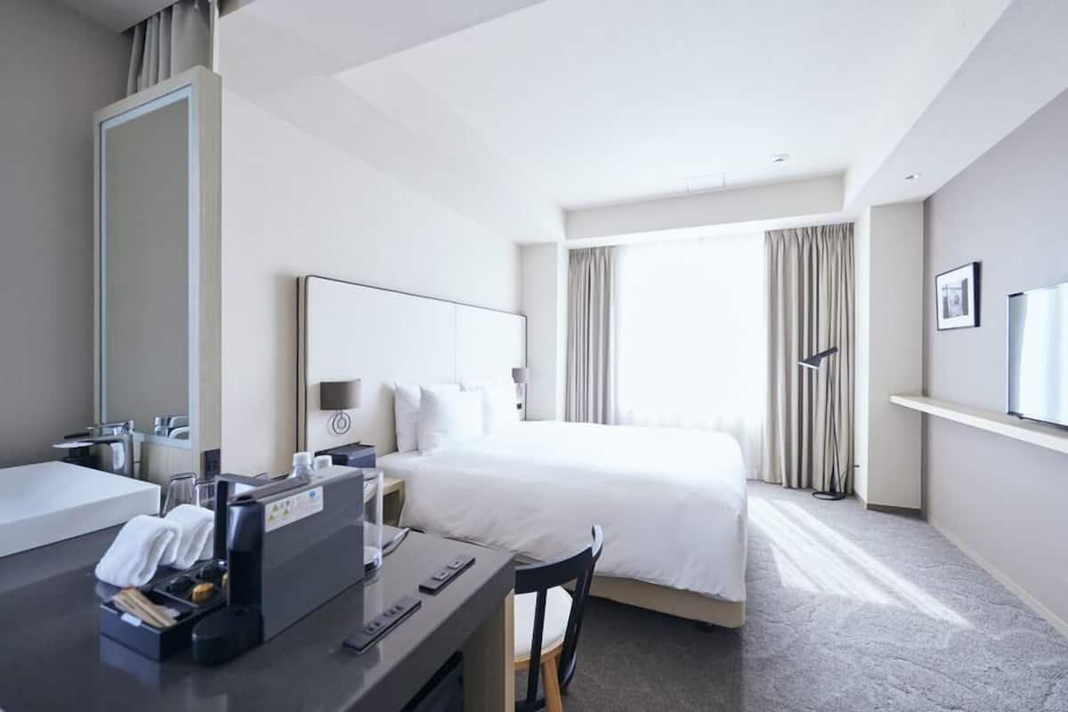 Habitación de hotel con una cama, un escritorio con computadora, un espejo y una ventana con cortinas.