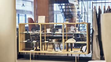 Zona de recepción de un hotel con un expositor de madera que contiene varios objetos, un letrero que indica que es un hotel certificado, y vista del interior a través de un ventanal.