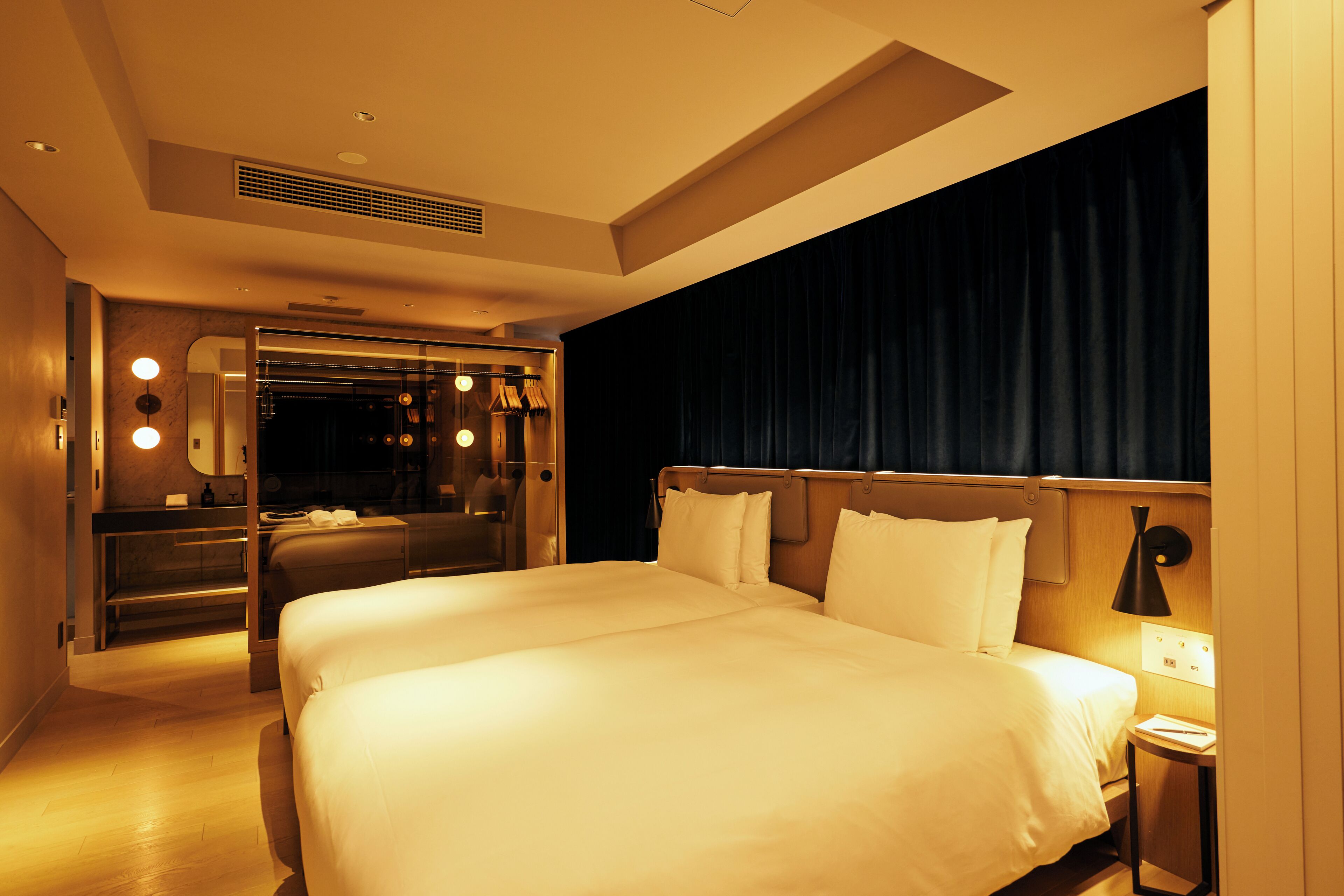 A hotel room with a large bed, a mirror, a vanity with lights, and a dark curtain.