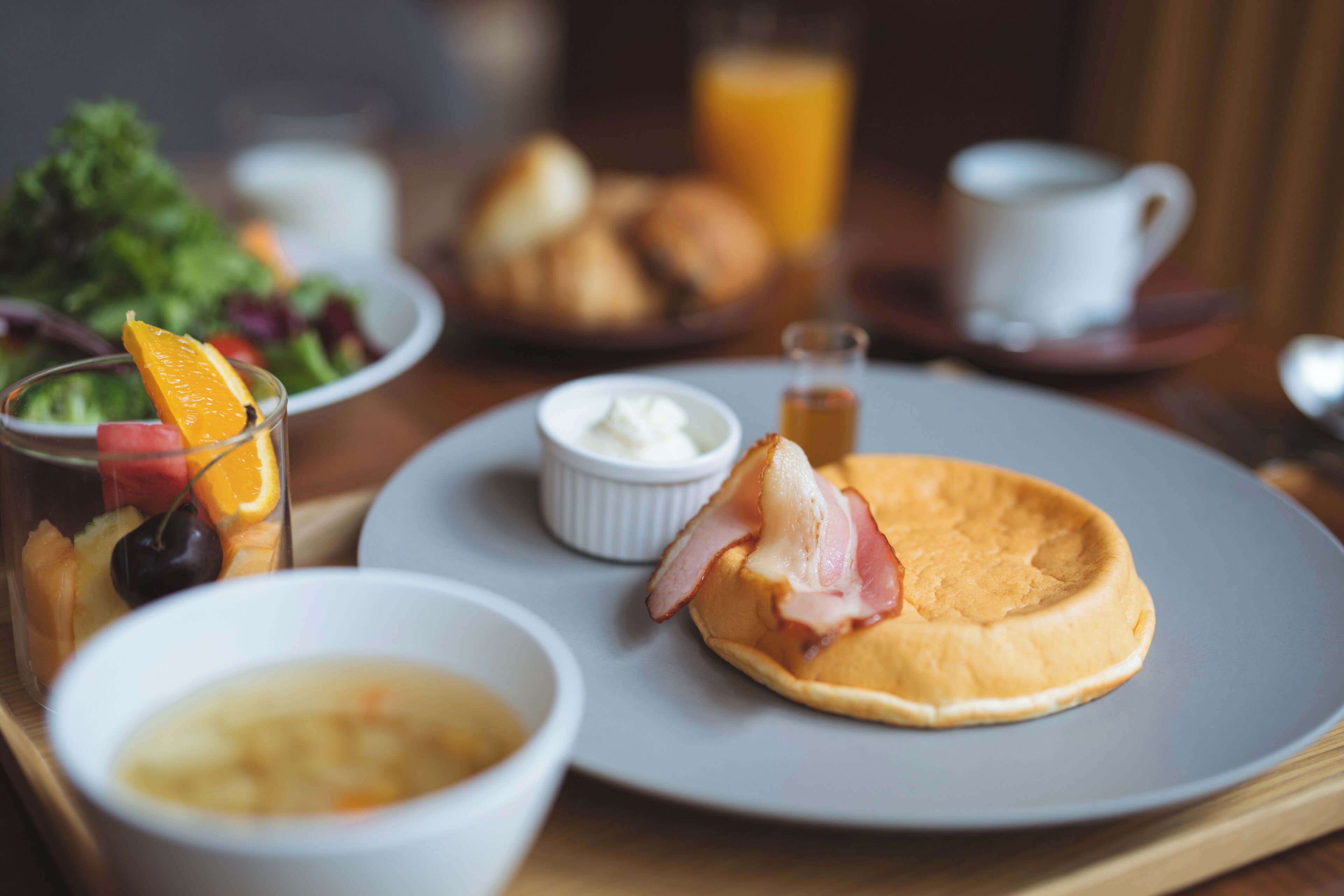 A breakfast tray with a plate of eggs, a bowl of soup, a glass of orange juice, and a salad.