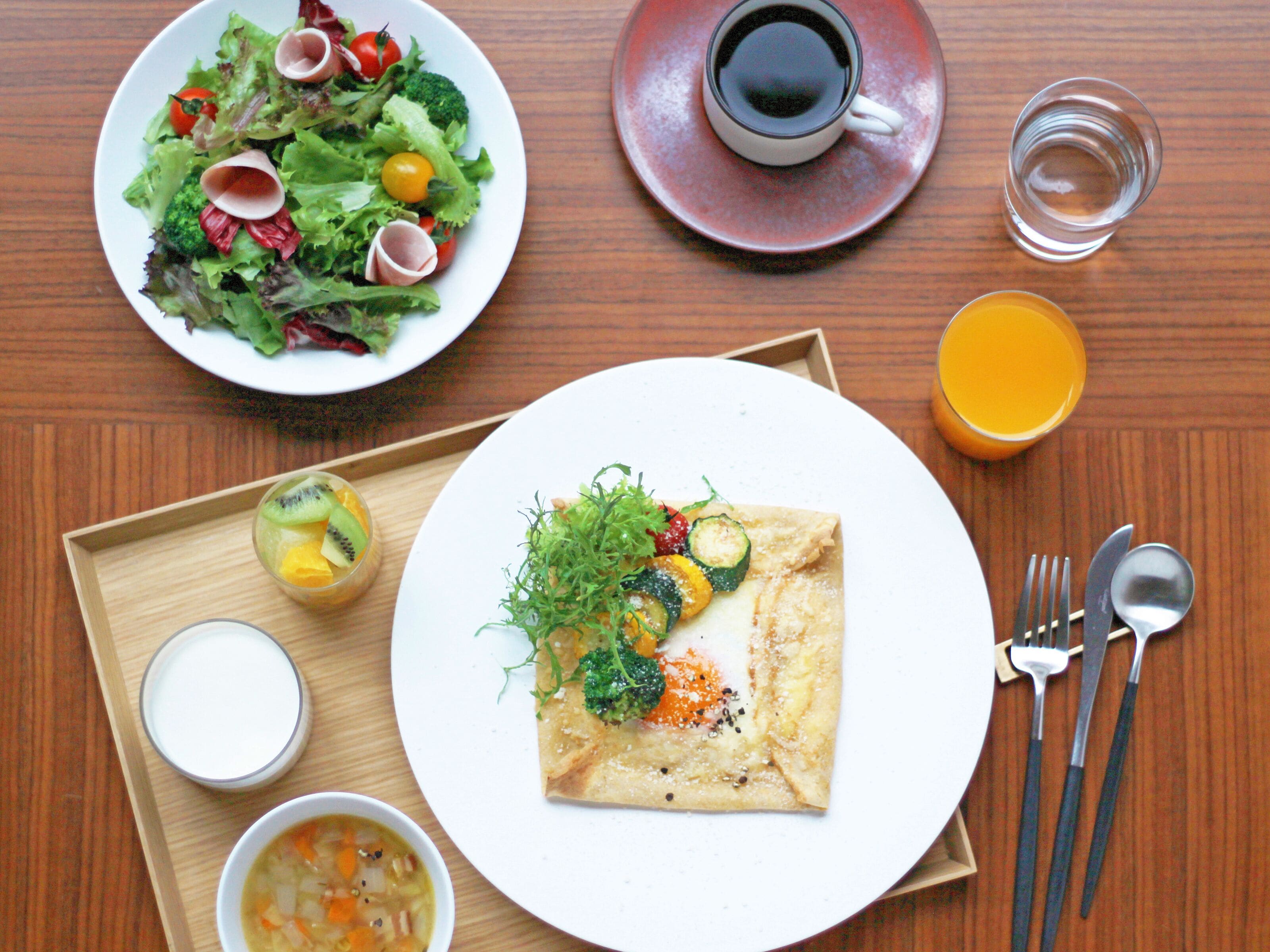 A meal with a salad, soup, and a rolled dish on a wooden table.