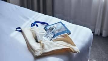 A neatly made bed with a white sheet, a blue pillow, a white pillowcase, a clear water bottle, and a blue booklet on the bed.