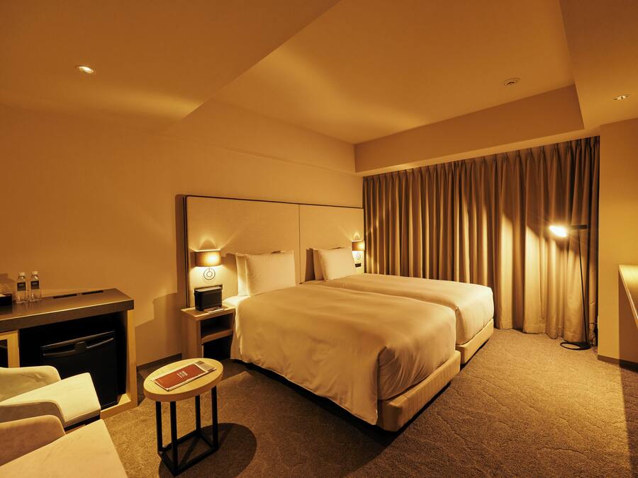 Ein Hotelzimmer mit einem großen Bett, einem Schreibtisch mit Stuhl, einem kleinen runden Tisch und einem Fernseher.