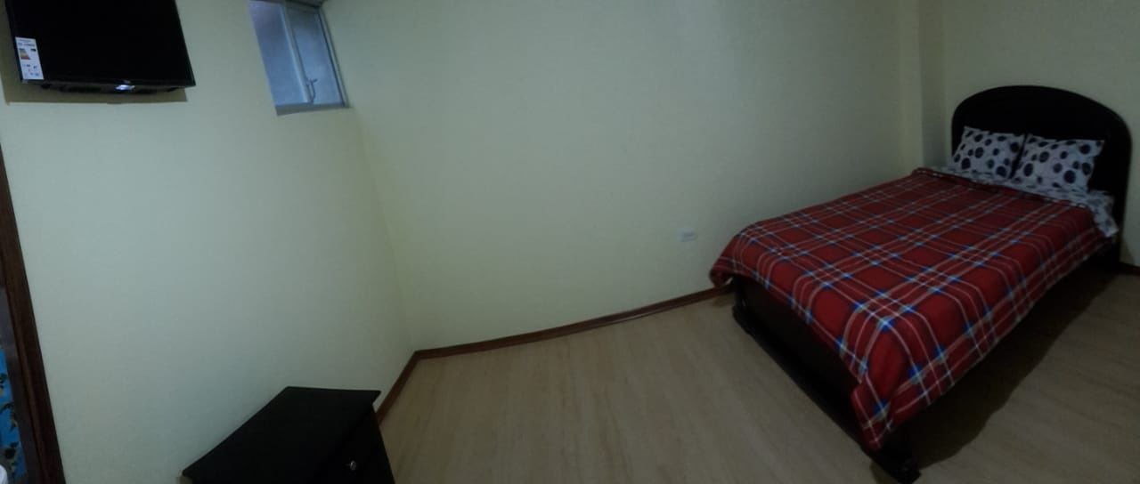 Un dormitorio con una cama, un ventanal pequeño y un televisor en la pared.