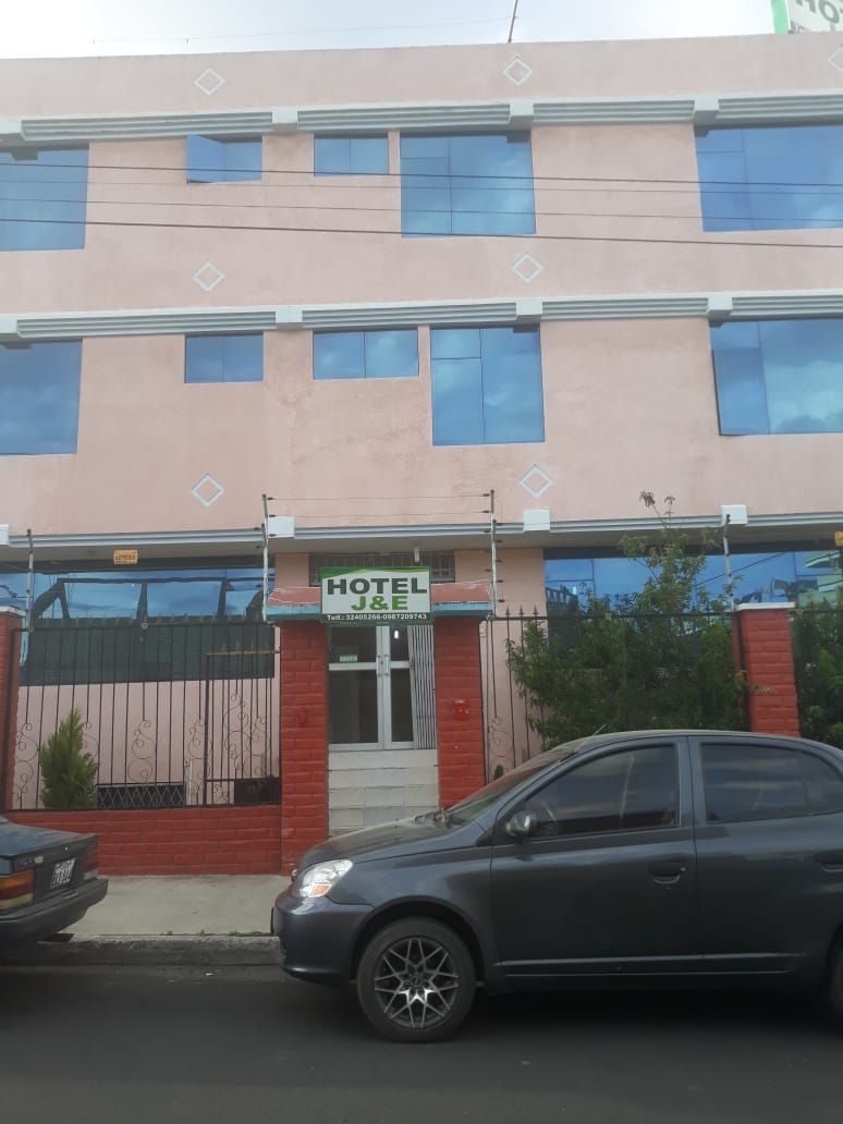 Edificio de hotel con un cartel, una entrada con portón y un coche estacionado.