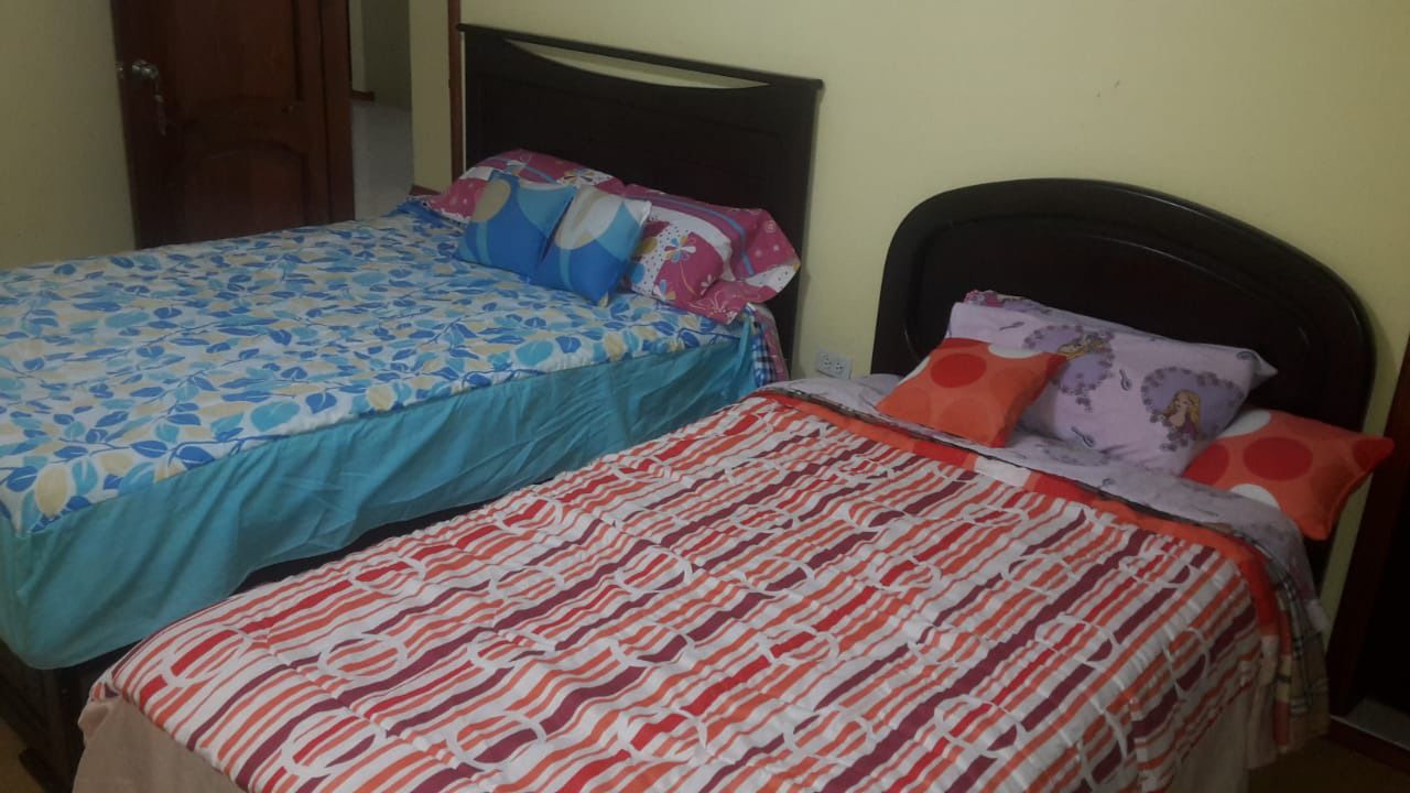 Two single beds with different patterned bedspreads, a wooden headboard, and a door in the background.