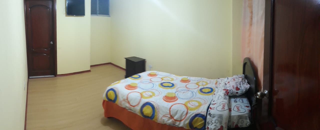 Un dormitorio con cama, una puerta de madera, una mesita de noche pequeña y una ventana.
