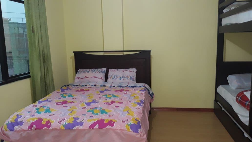 Un dormitorio con una cama, una litera, una ventana con cortina y una pared lisa.