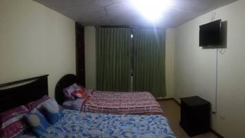 Un dormitorio con cama, televisor, cortina y una pequeña mesa.