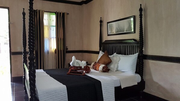 A four-poster bed with a headboard, a wooden nightstand, and a framed picture above it. - Country Inn Hotel Baggao- Main (Baggao)