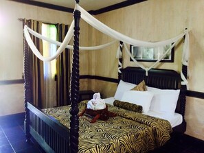 A four-poster bed with a zebra-patterned bedspread, a wooden headboard, and a window with curtains. - Country Inn Hotel Baggao- Main (Baggao)